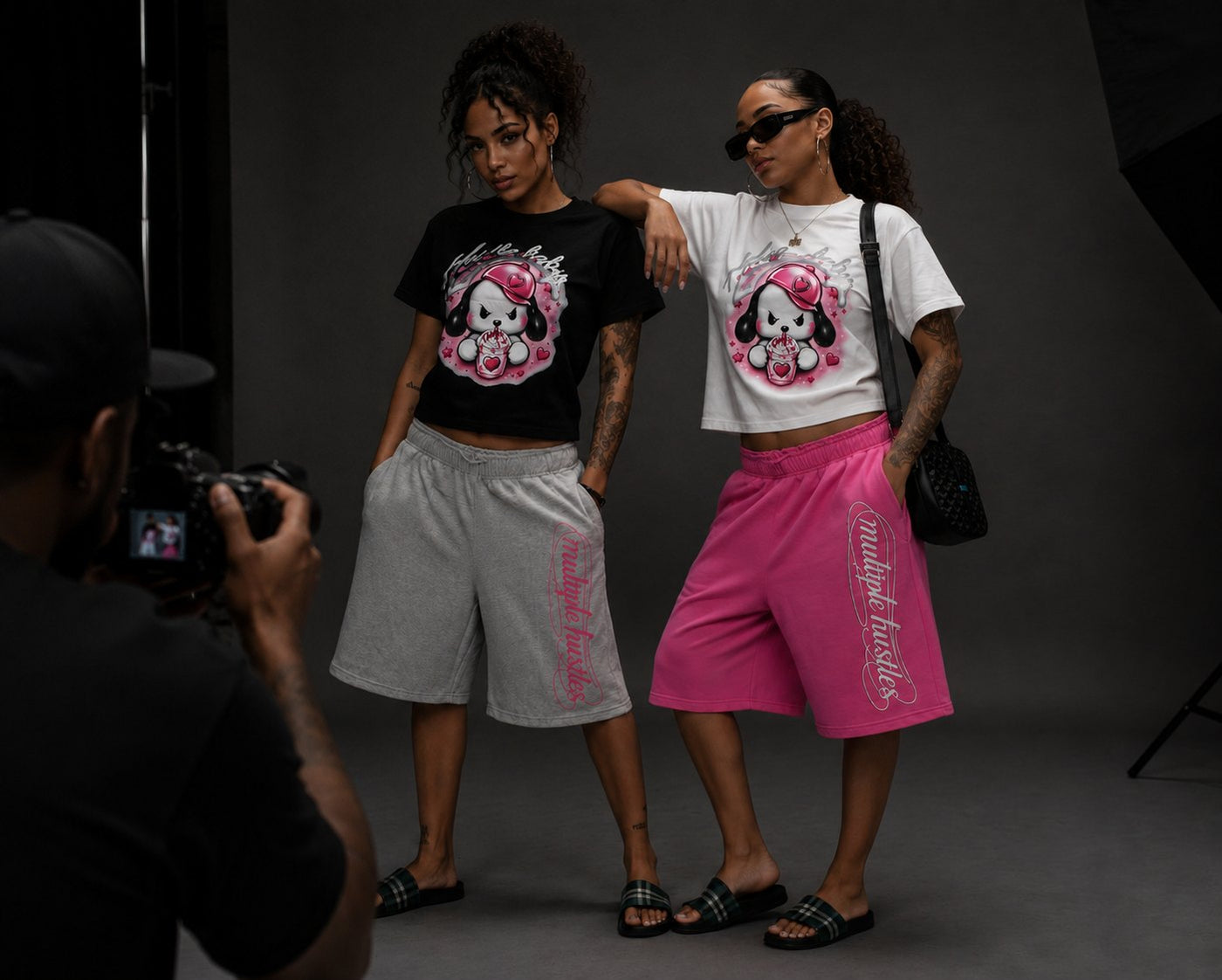 Two models on set wearing the Multiple Hustles shorts in grey and pink